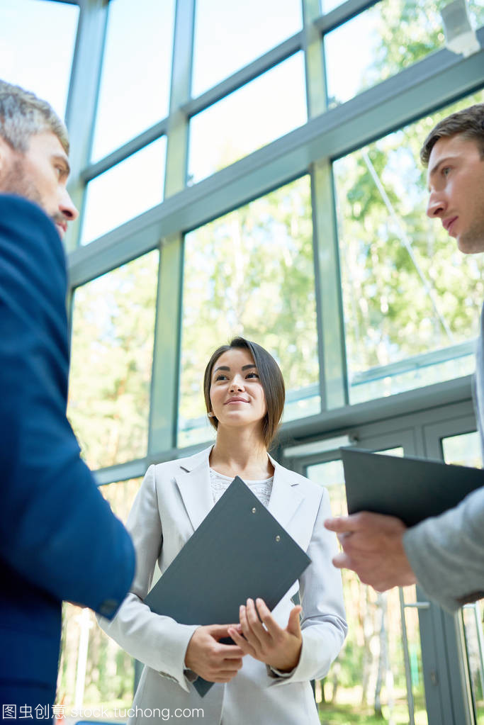 低角度觀在成功的企業家群藏品板站立在現代辦公室大廈大廳談論工作, 注重微笑的亞洲女實業家